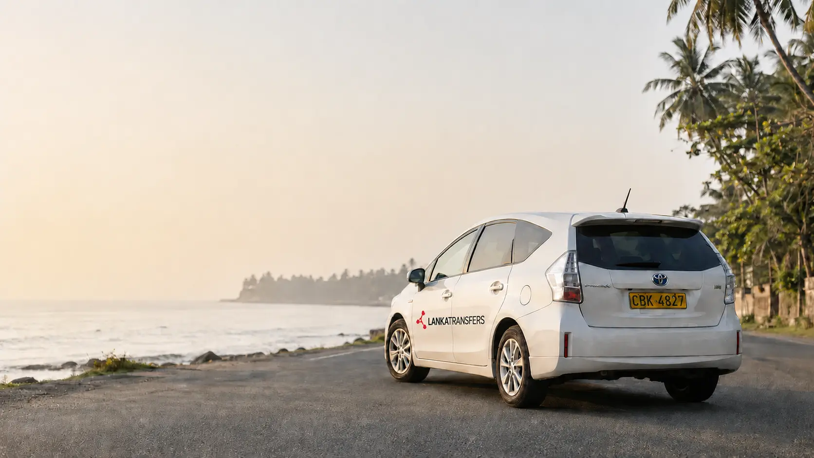 A branded LankaTransfers Toyota Prius Alpha ready for a popular fixed-price transfer on a Sri Lankan coastal road